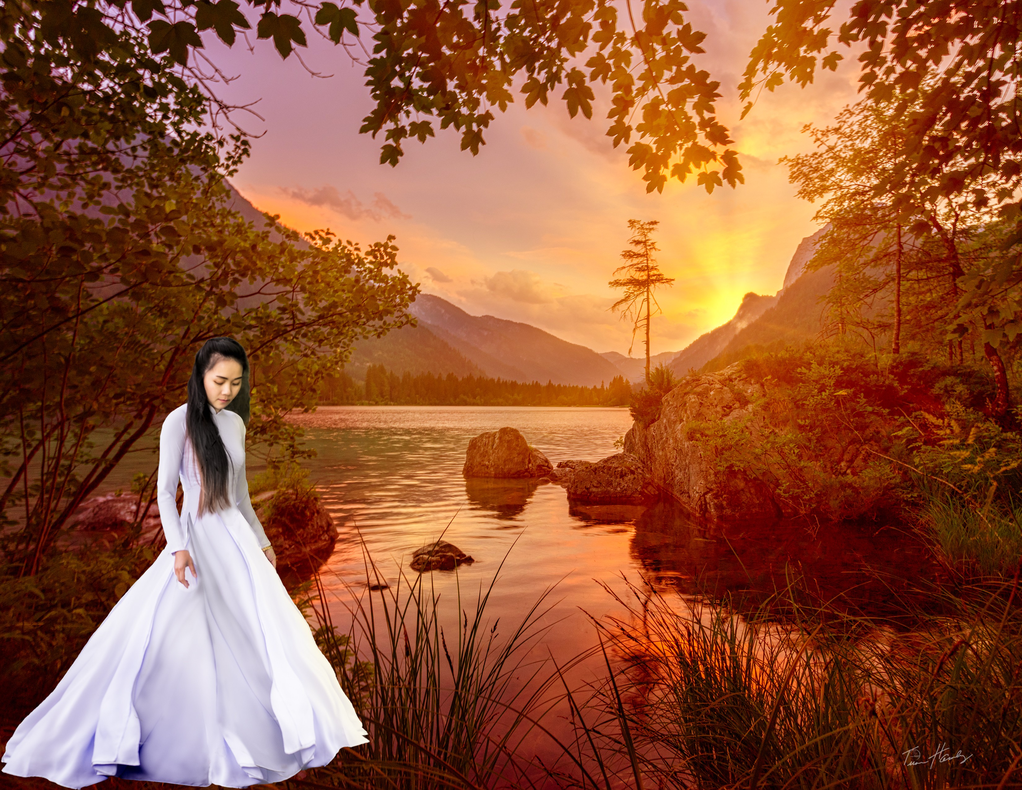 Woman in áo dài standing by mountain lake at sunset